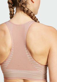 Sujeción deportiva de color rosa claro con textura acanalada, que presenta un diseño de espalda nadadora y patrones lineales sutiles en los hombros y la espalda.
