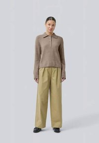 Pull en tricot marron avec un col et quatre boutons, associé à un pantalon kaki taille haute et à jambes larges, et des chaussures noires.