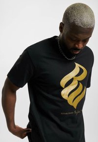 Black t-shirt featuring a shiny gold flame design and text at the bottom. Made from cotton, it has a regular fit and short sleeves.