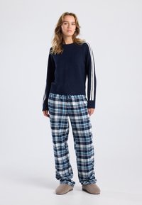 Navy sweater with white stripes, paired with blue and white plaid flannel pants. Soft texture, relaxed fit, and comfortable footwear.
