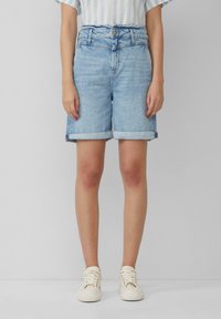 Světle modré džíny šortky s ohrnutým lemem, na knoflík a s poutky na opasek. Nosené s pruhovaným topem a bílými teniskami.