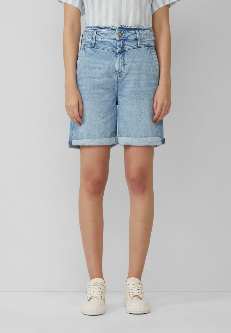 Světle modré džíny šortky s ohrnutým lemem, na knoflík a s poutky na opasek. Nosené s pruhovaným topem a bílými teniskami.