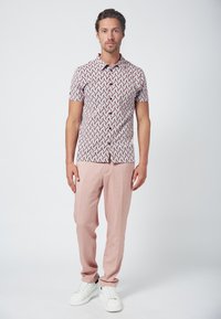 Camisa de manga corta con un patrón geométrico en rojo, rosa y blanco, combinada con pantalones rosa claros y zapatillas blancas.