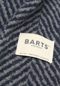 Marineblauwe en grijze stof met een zigzagpatroon en een zachte textuur; bevat een wit genaaid label met de tekst "BARTS AMSTERDAM" en "EST. 1992".