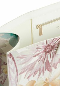 Interno di una borsa color crema chiaro con stampe floreali in rosa e verde. Include una tasca con cerniera e dettagli in oro. Tessuto strutturato.