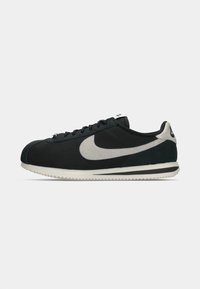 Sorte ruskindssneakers med et gråt swoosh, hvid gummisål, rund tå og teksturerede detaljer. Klassisk design med lav profil.