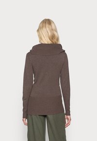 Brązowy sweter z dzianiny z szerokim kołnierzem, prążkowanym dołem i mankietami, dopasowany krój, zestawiony z luźnymi zielonymi spodniami.