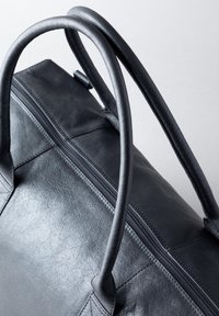 Black leather tote bag with smooth texture, dual rounded handles, and a top zipper closure. Features subtle stitching details.