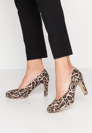 Højhælede sko med leopardprint, rund tå, beige bund og en kraftig hæl, vist sammen med sorte korte bukser på en hvid baggrund.