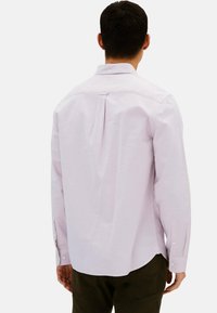Camicia a maniche lunghe di colore viola chiaro con piega sul retro, colletto standard e polsini con bottoni. Realizzata in tessuto liscio, tagliata leggermente più lunga sul retro.