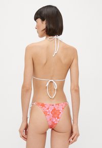 Bikini deux pièces : haut blanc à encolure halter avec liens ajustables, présentant un bas à motif floral rose avec des liens sur les côtés et une coupe taille basse.