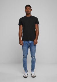 Camiseta de algodón negra de mangas cortas, combinada con jeans de mezclilla claros y desgastados. Zapatillas deportivas casuales con toques en blanco y gris.