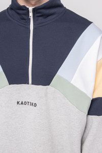 Halv-zip genser i marineblå og pastelldfarger, med en blanding av bomull og polyester. "KAOTIKO"-logo brodert på grå seksjon. Struktureret stoff.