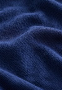 Tessuto di un blu scuro, texturizzato con una superficie morbida e liscia; leggere ondulazioni e pieghe creano profondità nell'aspetto.