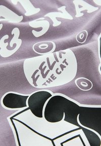 Lila tyg med vita och svarta tecknade kattspår, texten "Felix the Cat," och abstrakta ringar tryckta på.