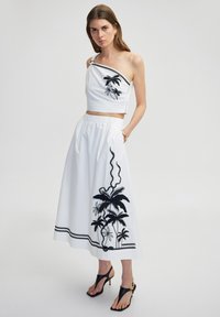 Bílý crop top s jedním ramínkem, zdoben�ý černou výšivkou palmy. Ladící bílá sukně s černými vzory palmy a lana, elastický pas.