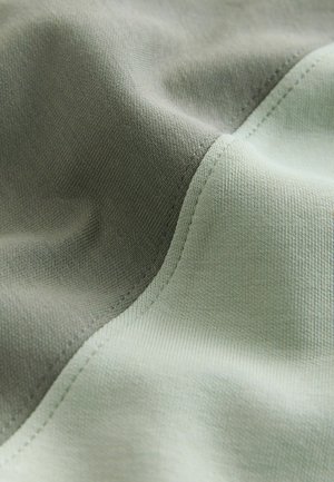 Minkšta medžiaga su žalia ir švelnia pilka spalvų blokų kompozicija. Lygi tekstūra, vientisa išlenkta kraštinė ir smulkios siūlės.