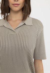 Lichtgrijze geribbelde gebreide top met een kraag, korte mouwen en een gestructureerde afwerking. Heeft verticale strepen en een subtiele glans.