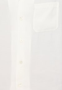 Cămașă albă cu nasturi, confecționată dintr-un material neted; prezintă un singur buzunar pe piept și cinci nasturi pe față pentru închidere.