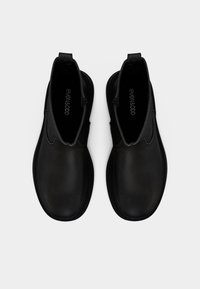 Ζευγάρι μαύρα δερμάτινα μποτάκια αστραγάλου με στρογγυλεμένες μύτες, πλαϊνά φερμουάρ και θηλιές, απεικονισμένα από πάνω σε λευκό φόντο.