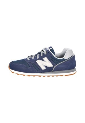 Zapatilla de ante azul marino y malla con cordones grises, logo blanco "N" en el lateral, cuello acolchado y suela de goma.
