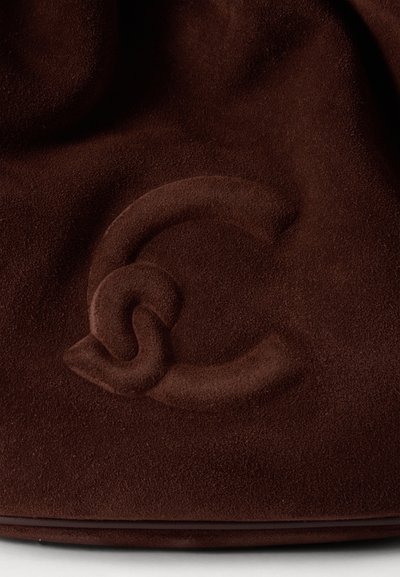 Gros plan sur un matériau en daim marron foncé avec un logo double C entrelacé embossé.