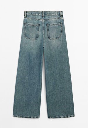 Hoch taillierte, weit geschnittene blaue Jeans mit Gesäßtaschen, Gürtelschlaufen und kontrastierenden Nähdetails, flach auf einem weißen Hintergrund ausgelegt.
