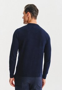 Granatowy sweter z długimi rękawami i okrągłym dekoltem, wykonany z gładkiej dzianiny, z prążkowanymi mankietami i dołem.