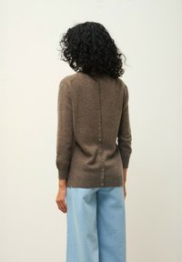 Brun stickad tröja med rund halsringning, knappstängning bak och trekvartsärmar, i kombination med ljusblå vida byxor.