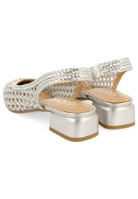 Sandalias plateadas trenzadas con un tacón grueso de plataforma metálica, diseño de punta abierta y una plantilla beige suave; detalle de correa ajustable.