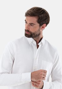 Weißes Button-up-Hemd aus Baumwolle mit einer Brusttasche, langen Ärmeln und einem klassischen Kragen mit Knopfverschluss.