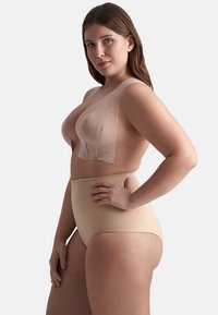 Reggiseno beige senza cuciture con spalline larghe e scollatura bassa abbinato a shapewear color nude a vita alta. Texture liscia, design minimalista.