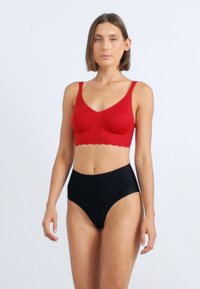 Rød tekstureret bralette med brede stropper og bølget kant, parret med højtaljede sorte trusser. Glat, strækbart stof.