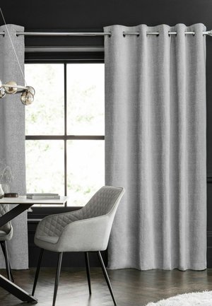 Zona pranzo moderna con sedia grigia trapuntata, finestra con cornice nera, tende grigio chiaro e pavimento in legno scuro.