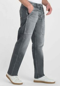 Jeans in denim grigio con una vestibilità rilassata, dotati di due tasche anteriori, una tasca posteriore e cuciture a contrasto. Abbinati a sneaker bianche.