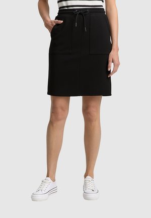 Schwarze Hose mit elastischem Bund und Kordelzug, ausgestattet mit zwei vorderen Taschen. Kombiniert mit weißen Sneakers für einen lässigen Look.