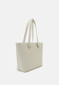 Sac fourre-tout en cuir couleur crème avec doubles anses d'épaule et œillets métalliques argentés sur fond blanc uni.