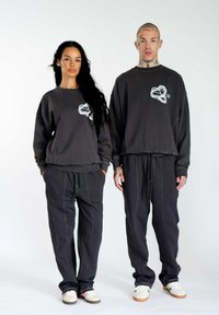 Schwarz-graue Sweatshirts mit Grafiklogo, kombiniert mit lockeren Sweatpants mit weißem Kontraststich. Legere Schuhe inklusive.