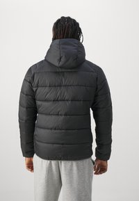 Czarna kurtka puchowa z kapturem, z pikowanym wzorem, teksturowanym wykończeniem i elastycznymi mankietami, noszona z szarymi dresami.