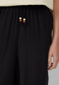 Schwarze, leichte Hosen aus strukturiertem Stoff, mit einem Kordelzugbund und Akzentperlen in Creme- und Holztönen.