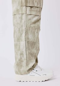 Lichtgroene, gestructureerde broek met zijzakken, gecombineerd met witte sneakers met zwarte accenten en dikke zolen.
