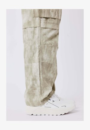 Lichtgroene, gestructureerde broek met zijzakken, gecombineerd met witte sneakers met zwarte accenten en dikke zolen.
