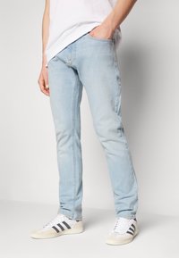 Hellblaue Jeans mit geradem Bein, ausgestattet mit fünf Taschen und dezenten Nähdetails. Kombiniert mit weißen Sneakers.