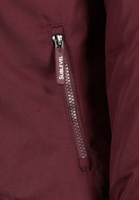Burgundy jacket featuring a side zip pocket with a silver metal zipper and a branded pull tab. Smooth texture and lightweight fabric.