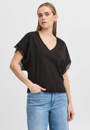 Zwarte v-hals top met korte dolman mouwen en kantafwerking. Zachte textuur, losse pasvorm, gecombineerd met lichtblauwe spijkerbroek.