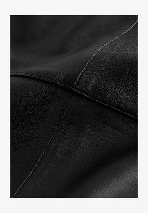 Nahaufnahme von schwarzem Leder mit sichtbar feiner Körnung und sich kreuzenden genähten Nähten, die Paneele bilden.