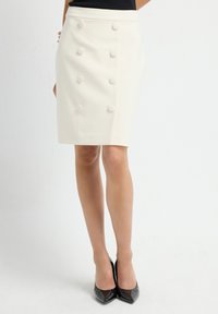 Witte op maat gemaakte kokerrok met een hoge taille en zes ronde, met stof beklede knopen aan de voorkant, gecombineerd met zwarte hoge hakken.