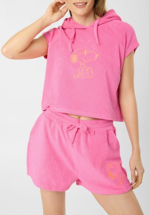 Vrouw draagt een roze mouwloos hoodie- en shortset met gele Snoopy-illustraties op de borst en linker dij.