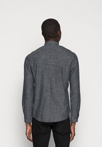 Langarmshirt in donkergrijs, met een gestructureerde stof. Voorzien van een gebogen zoom, knopenmanchetten en een staande kraag. De achterkant toont naaddetails.