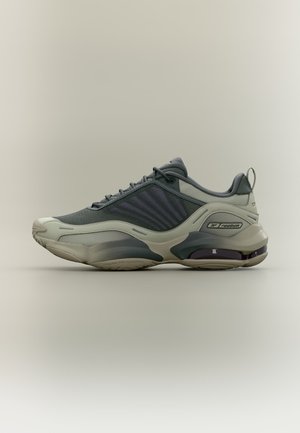 Šedý a béžový atletický teniska Reebok s horní částí z síťoviny, polstrovanou podrážkou a poutkem, zobrazená z boku na neutrálním pozadí.